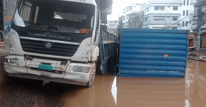 ভাঙা সড়কে উল্টে গেছে কন্টেইনারবাহী লরি